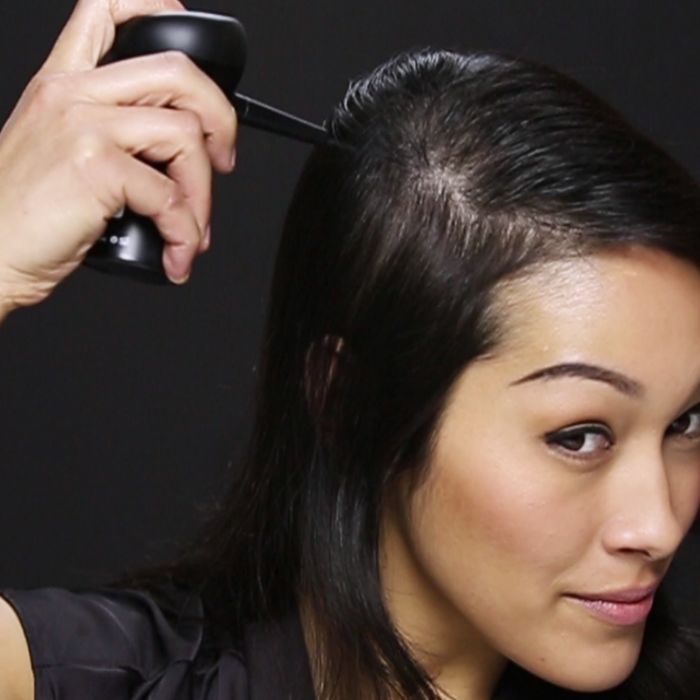 woman using Toppik hair building fiber with spray applicator 