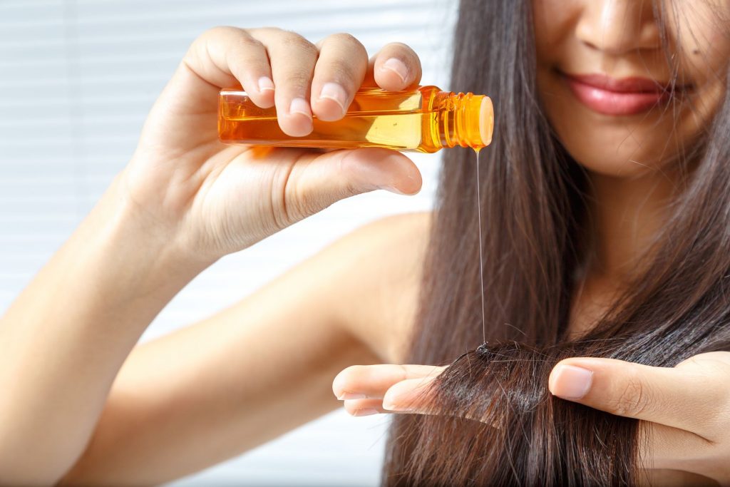 woman pouring rosemary oil for hair growth on her long hair