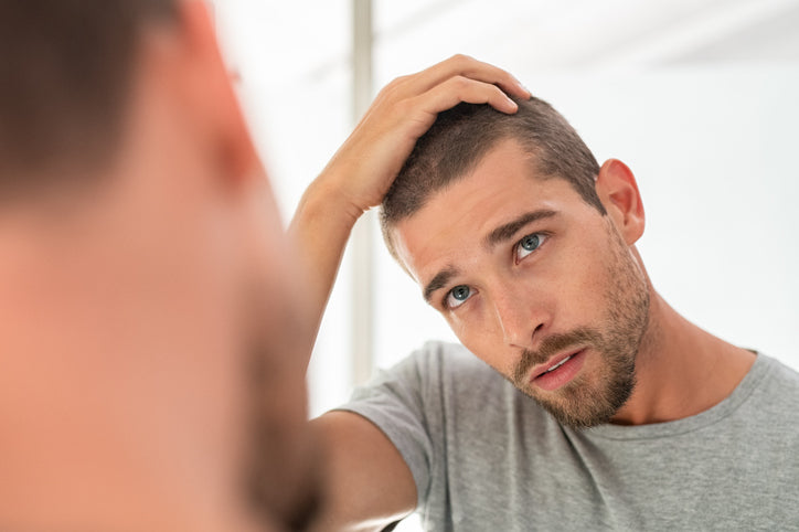 Man looking in the mirror while inspecting his hairline.