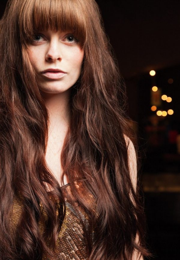 Closeup woman red auburn long hair bangs dark black background brown sequin shirt haircuts for long thin hair toppik hair blog