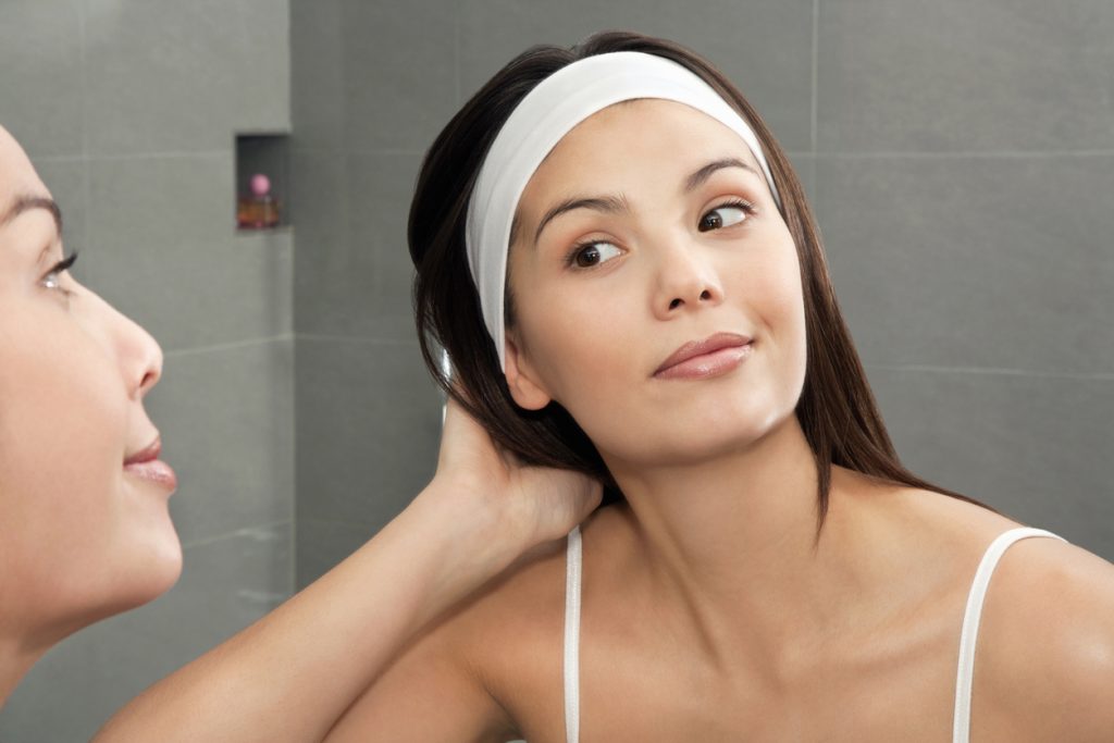 A dark-haired woman looks in the mirror, about to create heatless curls in her hair.
