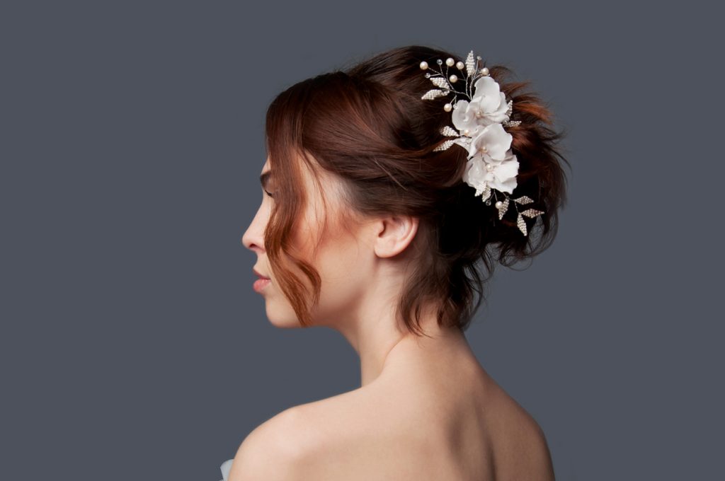Side view of a bride, her dark brown hair twisted in an updo, accented by white silk bead pearl flowers for her wedding day.