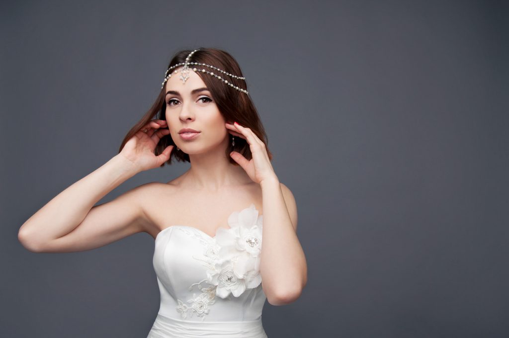 A bride with thin brown hair wears it in a short bob wedding hairstyle, accented nicely by a multi-strand pearl headband.