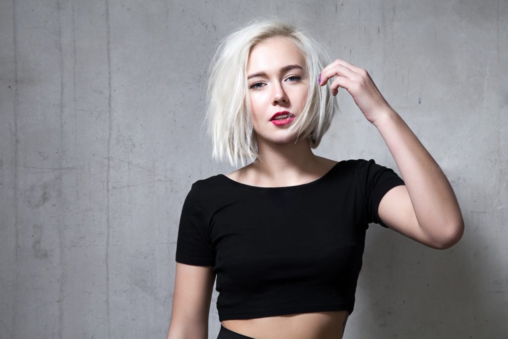 woman short bleach blonde bob hair red lips black shirt gray stone background tousle and go shag haircuts for men and women toppik hair blog