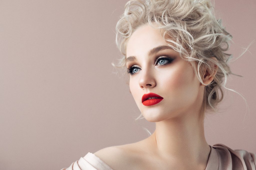 Closeup of a blonde bride wearing a curly updo wedding hairstyle and red lipstick