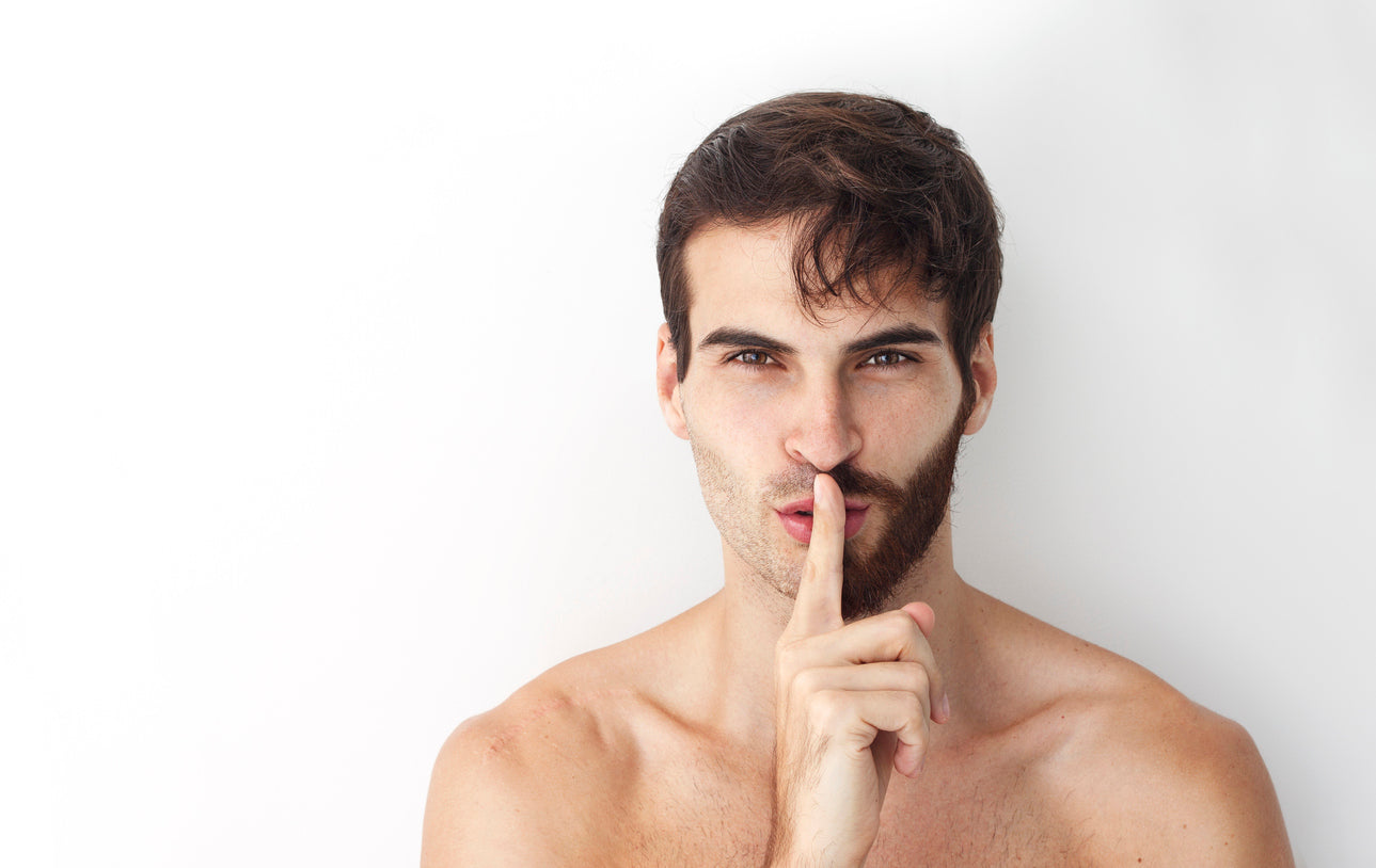 Man making a shushing gesture with half-cut hair and a half-trimmed beard.