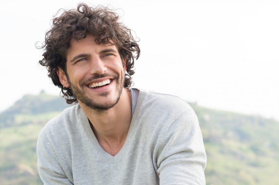 smiling handsome man brown curly hair outside mountain background 70s grow-out hairstyle 2020 hair trends for men and past styles toppik hair blog