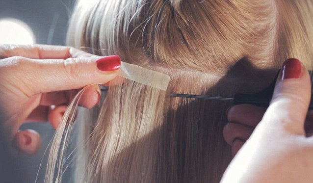 Woman getting tape-in hair extensions applied.