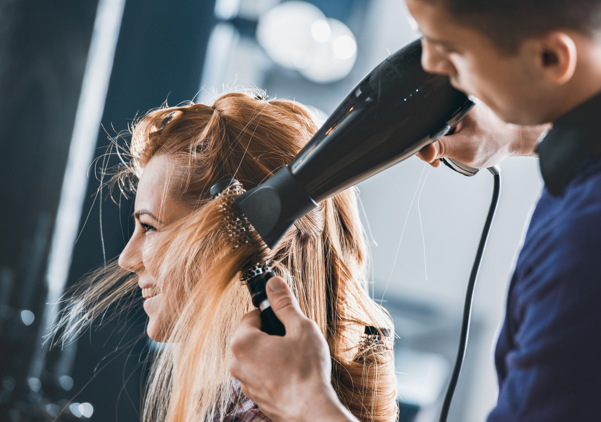 blow drying hair on smiling blonde woman side hair salon