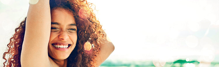 smiling woman curly hair arms up beach summer how to deal with humidity hair toppik hair blog