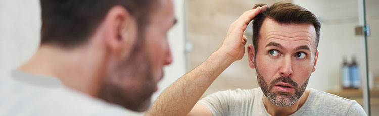 A man styles his hair in the mirror. How to add volume to thin hair.