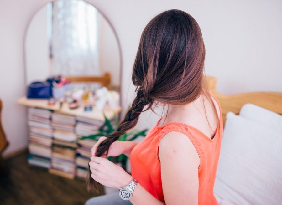 brunette woman braiding hair, bed back view. protect hair while sleeping toppik hair blog