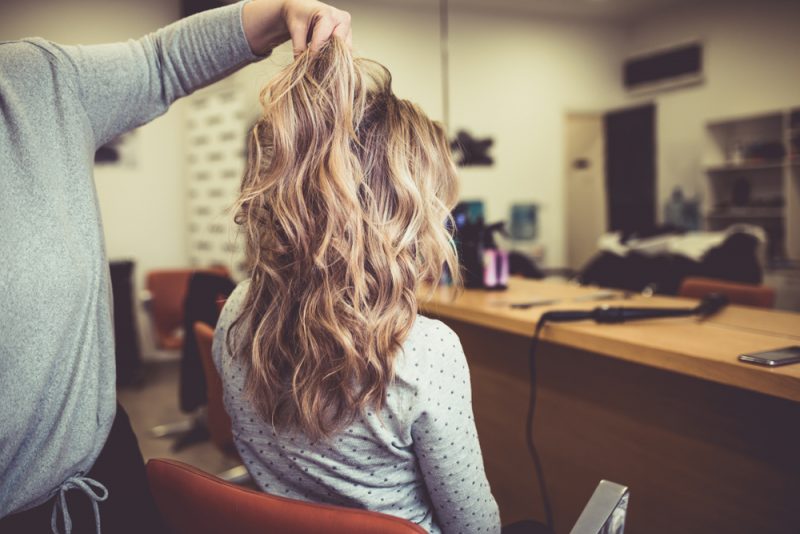 curly haired woman with highlights at hair salon  - What is sombre hair? 