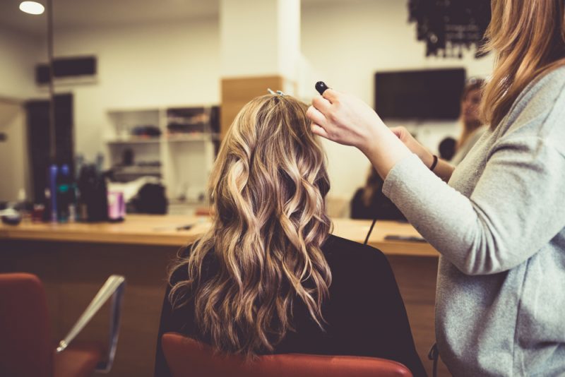 blonde curly hair woman salon chair back view stylist curling iron highlights hair dye how does hair toner work? toppik hair blog