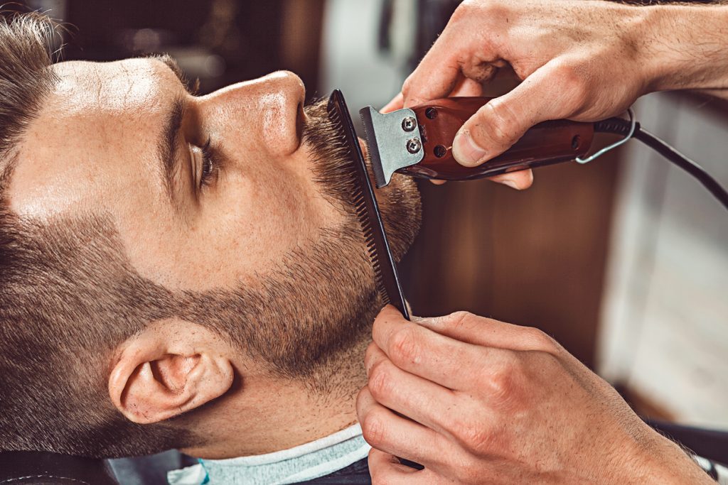 Man in barber shop gets beard trimmed and combed for movember or no-shave november challenge.