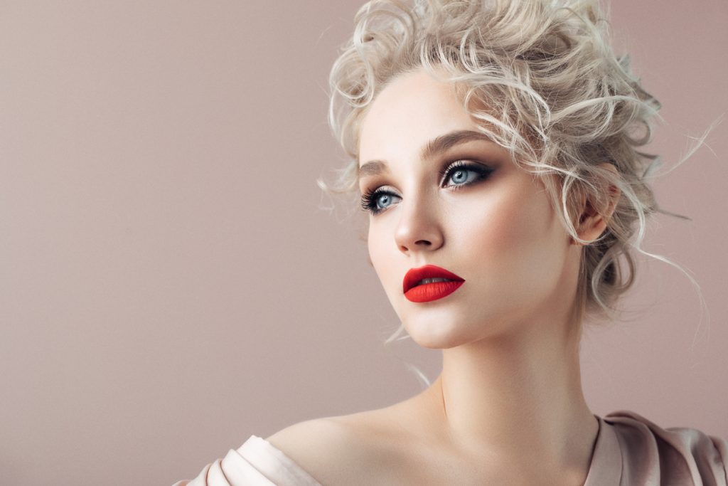 Closeup of a blonde bride wearing a curly updo wedding hairstyle and red lipstick
