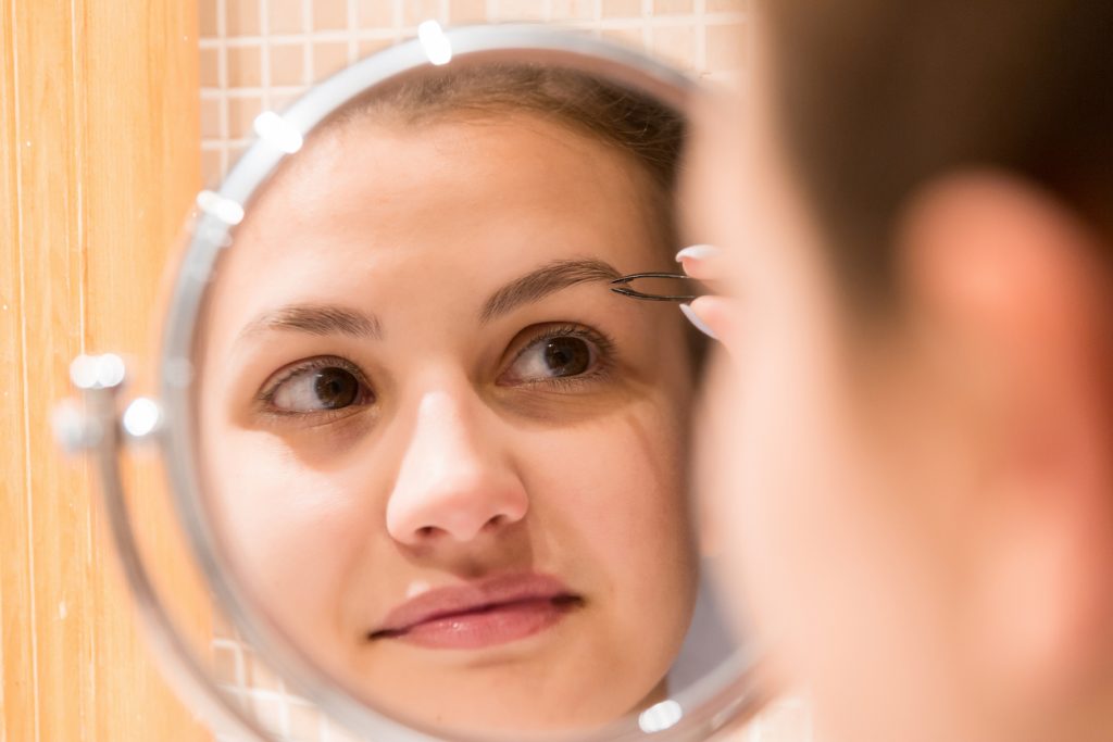 closeup woman pluck tweeze eyebrows magnifying bathroom mirror eyebrow styles in 2020 for you toppik hair blog